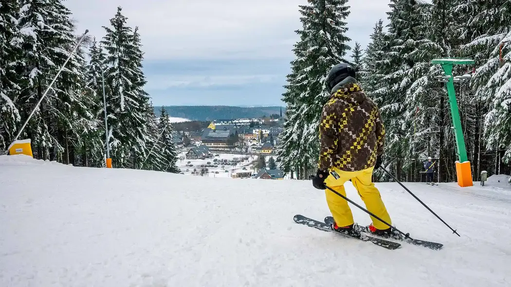 Ein junger Mann fährt mit Aussicht auf Altenberg die Skipiste hinunter