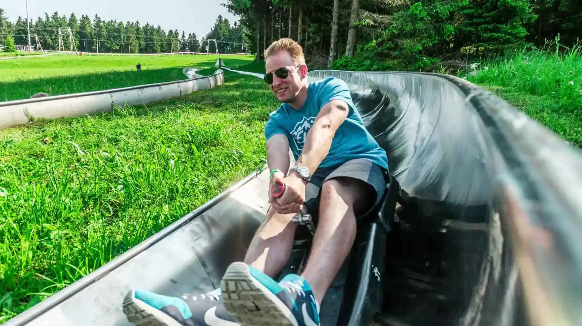 Ein junger Mann fährt schnell mit der Sommerrodelbahn in Altenberg durch die grüne Landschaft. Entdecken sie weitere spannenden Attraktionen am Erlebnisberg in Altenberg.
