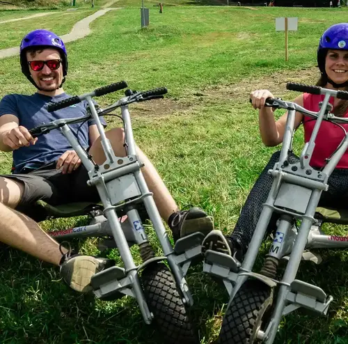 reisegruppen-altenberg-erzgebirge-sachsen-05.webp Ein Mann und eine Frau sitzen lachend in jeweils einem Mountaincart.