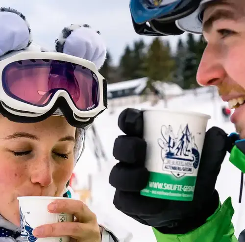 Ein junges Paar trinkt ein heißes Getränk in Skiausrüstung.