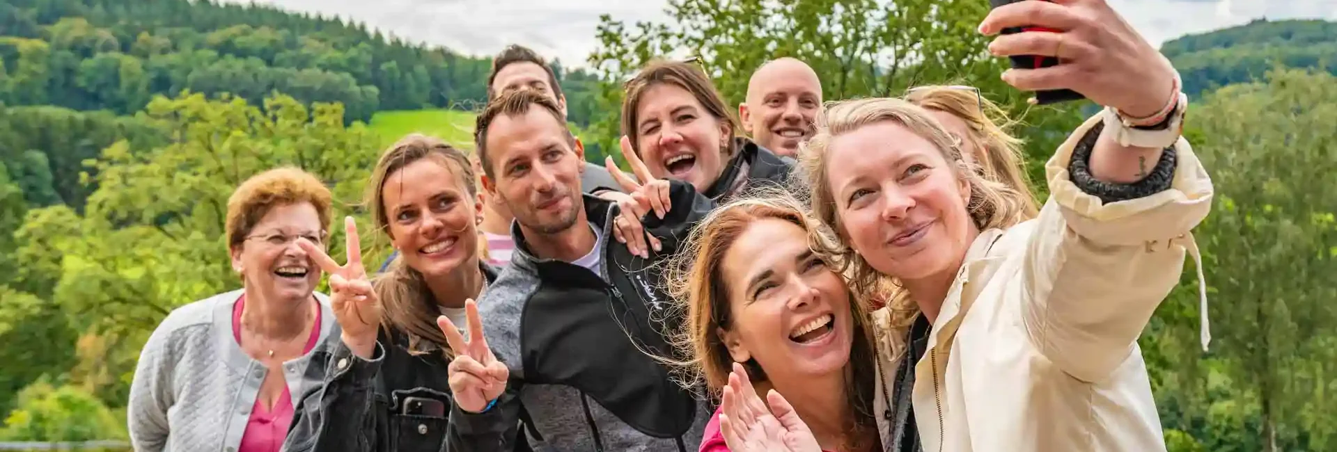 Eine junge Frau macht ein Selfie von sich und ihrer Reisegruppe. Alle sind am lachen und genießen die Natur. Erleben sie schöne Momente und tolle Gruppenangebote am Erlebnisberg in Altenberg.