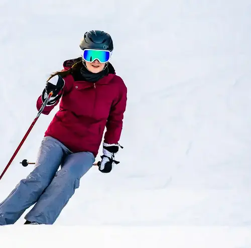 Eine Junge Dame fährt in Skiausrüstung eine verschneite Abfahrt herunter.