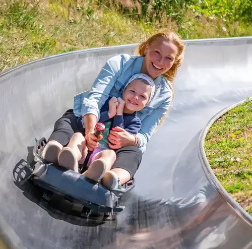 vereine-altenberg-erzgebirge-sachsen-29.webp Eine Frau fährt mit einem Kind die Sommerrodelbahn Freizeitpark Altenberg im Erzgebirge.
