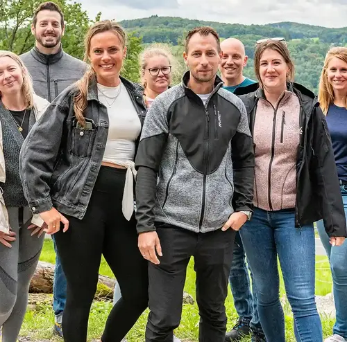 firmenevents-altenberg-erzgebirge-sachsen-23.webp Eine Gruppe von Menschen steht vor einer Kulisse mit Wolken und der grünen Natur am Freizeitpark Altenberg.