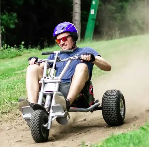 Ein junger Mann fährt mit einem Mountaincart durch die grüne Landschaft. Die steinige Strecke wirbelt Staub auf. Entdecken sie Natur und viele Attraktionen am Erlebnisberg in Altenberg.