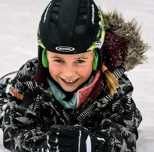 schulklassen-im-winter-altenberg-erzgebirge-sachsen-21.webp Ein Mädchen liegt lachend auf der Skipiste am Erlebnisberg Altenberg.