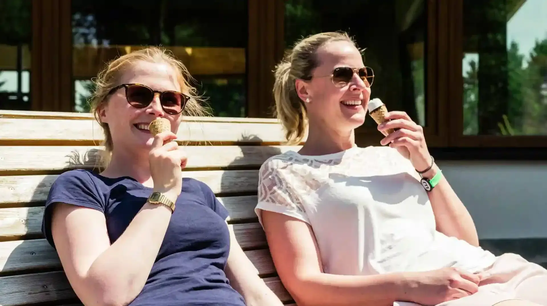 busreisen-altenberg-erzgebirge-sachsen-12.webp Zwei Frauen essen fröhlich ein Eis auf einer Bank am Erlebnisberg Altenberg.