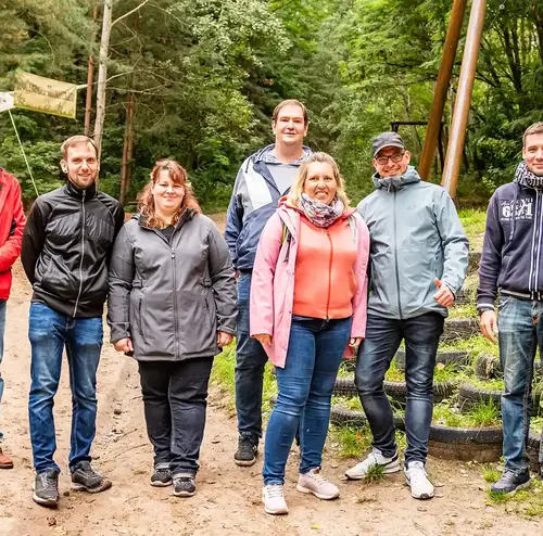 reisegruppen-altenberg-erzgebirge-sachsen-21.webp Eine Gruppe von Reisenden steht lächelnd inmitten eines Waldes am Erlebnisberg Altenberg.
