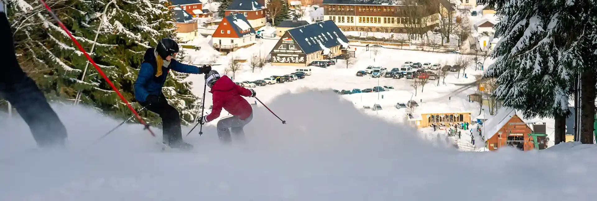 Man hat einen tollen Blick in das schöne Tal. Mehrere junge Skifahrer, fahren den Hang hinunter inmitten von verschneiten Bäumen. Sie fahren in Richtung der Talstation. Entdecken sie tolle Abfahren am Erlebnisberg Altenberg.