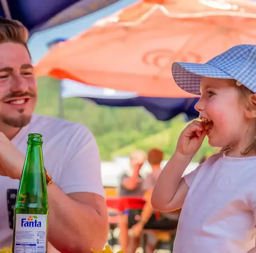 vereine-altenberg-erzgebirge-sachsen-21.webp Ein junger Mann und ein kleines Kind genießen eine Mahlzeit an der Rodelklause im Erzgebirge.