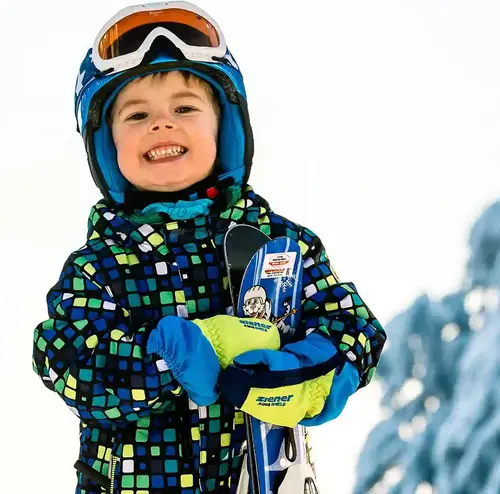 schulklassen-im-winter-altenberg-erzgebirge-sachsen-02.webp Ein kleiner Junge lacht in die Kamera während er die Skier des Erlebnisberg Altenberg in der Hand hält.