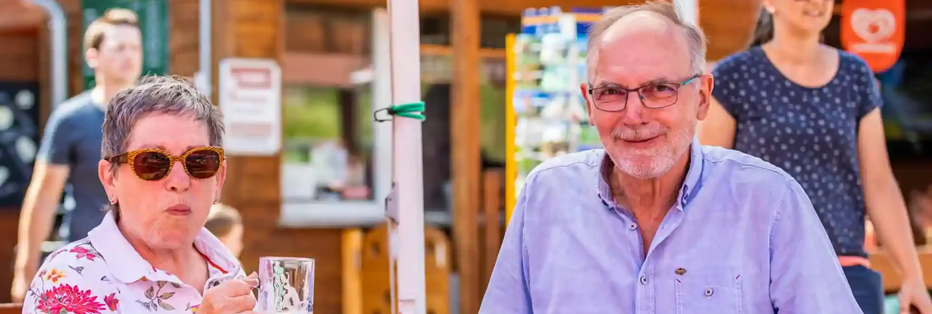 busreisen-altenberg-erzgebirge-sachsen-16.webp Ein Mann und eine Frau genießen ihr Essen und ein kühles Getränk an einer Hütte am Erlebnisberg Altenberg