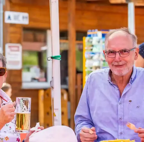 busreisen-altenberg-erzgebirge-sachsen-16.webp Ein Mann und eine Frau genießen ihr Essen und ein kühles Getränk an einer Hütte am Erlebnisberg Altenberg
