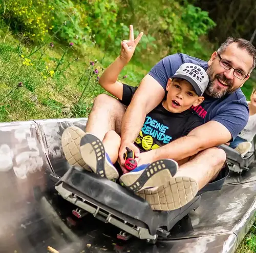 Ein Mann und ein Kind fahren mit der Sommerrodelbahn im Freizeitpark Erlebnisberg Altenberg.