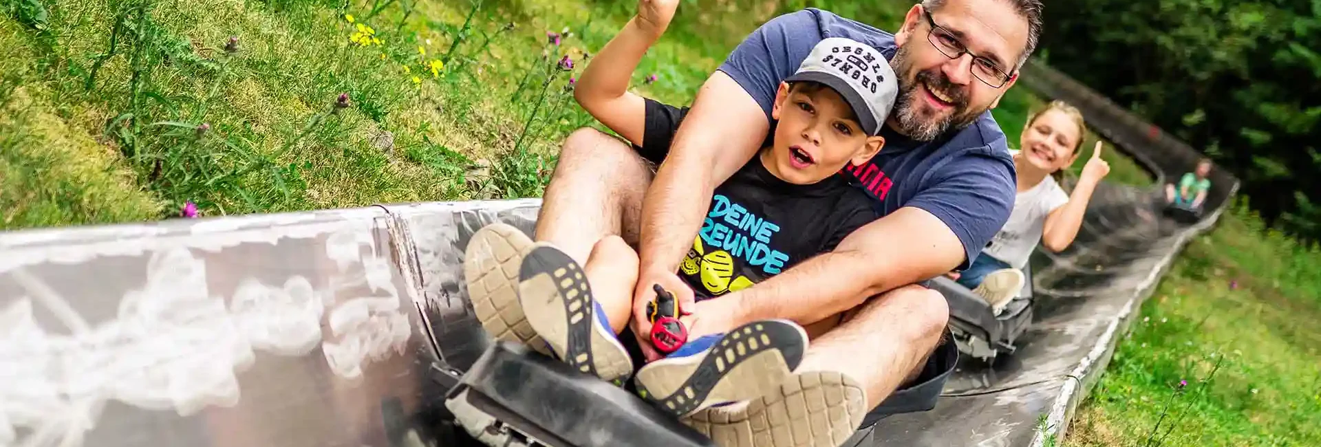 Ein Mann und ein Kind fahren mit der Sommerrodelbahn im Freizeitpark Erlebnisberg Altenberg.