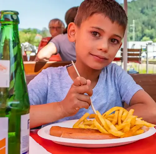 Ein Junge sitzt lächelnd an einem Tisch an der Rodelklause und isst sein Essen.