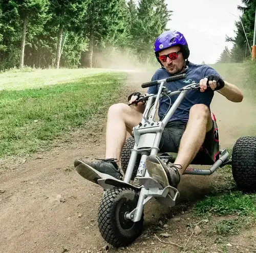 firmenevents-altenberg-erzgebirge-sachsen-03.webp Ein junger Mann fährt sichtlich konzentriert mit einem Mountaincart eine grüne Wiese hinunter.