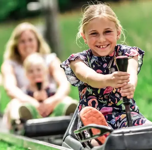 vereine-altenberg-erzgebirge-sachsen-08.webp Ein junges Mädchen fährt mit der Sommerrodelbahn und hält sich an der Bremse fest.