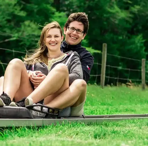 busreisen-altenberg-erzgebirge-sachsen-09.webp Ein Mann und eine Frau fahren mit der Sommerrodelbahn mit einer Kulisse voller grünen Bäume.