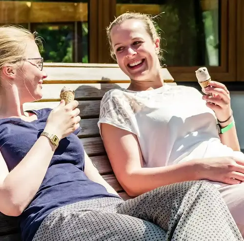 reisegruppen-altenberg-erzgebirge-sachsen-12.webp Zwei Frauen essen bei sommerlichem Wetter ein Eis am Erlebnisberg Altenberg.