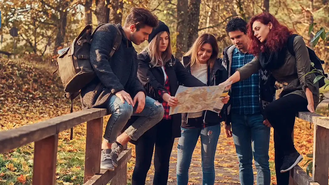 Eine Gruppe junger Erwachsener studiert eine Landkarte. Sie machen eine kurze Pause auf einer Brücke und genießen die Natur und die Sonne.
