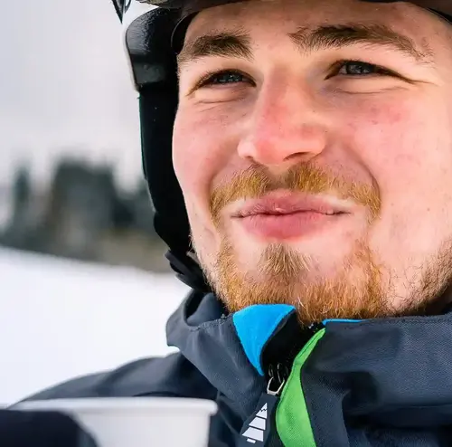 Ein junger Mann trinkt ein Heißgetränk. er trägt Skiausrüstung und schaut in die Ferne.
