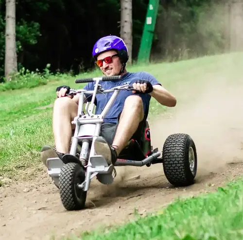 reisegruppen-altenberg-erzgebirge-sachsen-01.webp Ein Mann mit lilanem Helm fährt lachend mit dem Mountaincoaster den Skihang hinunter.