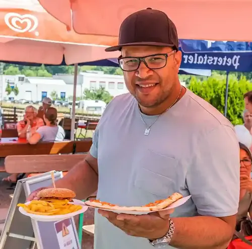 busreisen-altenberg-erzgebirge-sachsen-17.webp Ein Mann präsentiert glücklich sein Essen an der Rodelklause am Freizeitpark Altenberg.